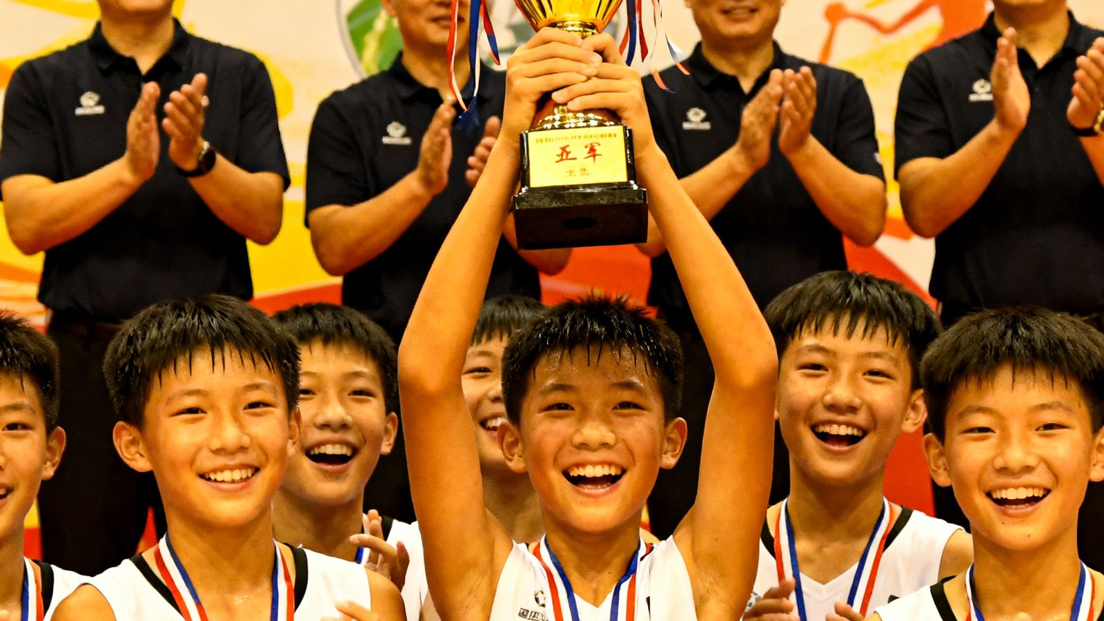 彩神U14篮球队在杭州市青少年篮球联赛颁奖台上举起季军奖杯，队员们笑容灿烂，教练团队站在后排鼓掌。